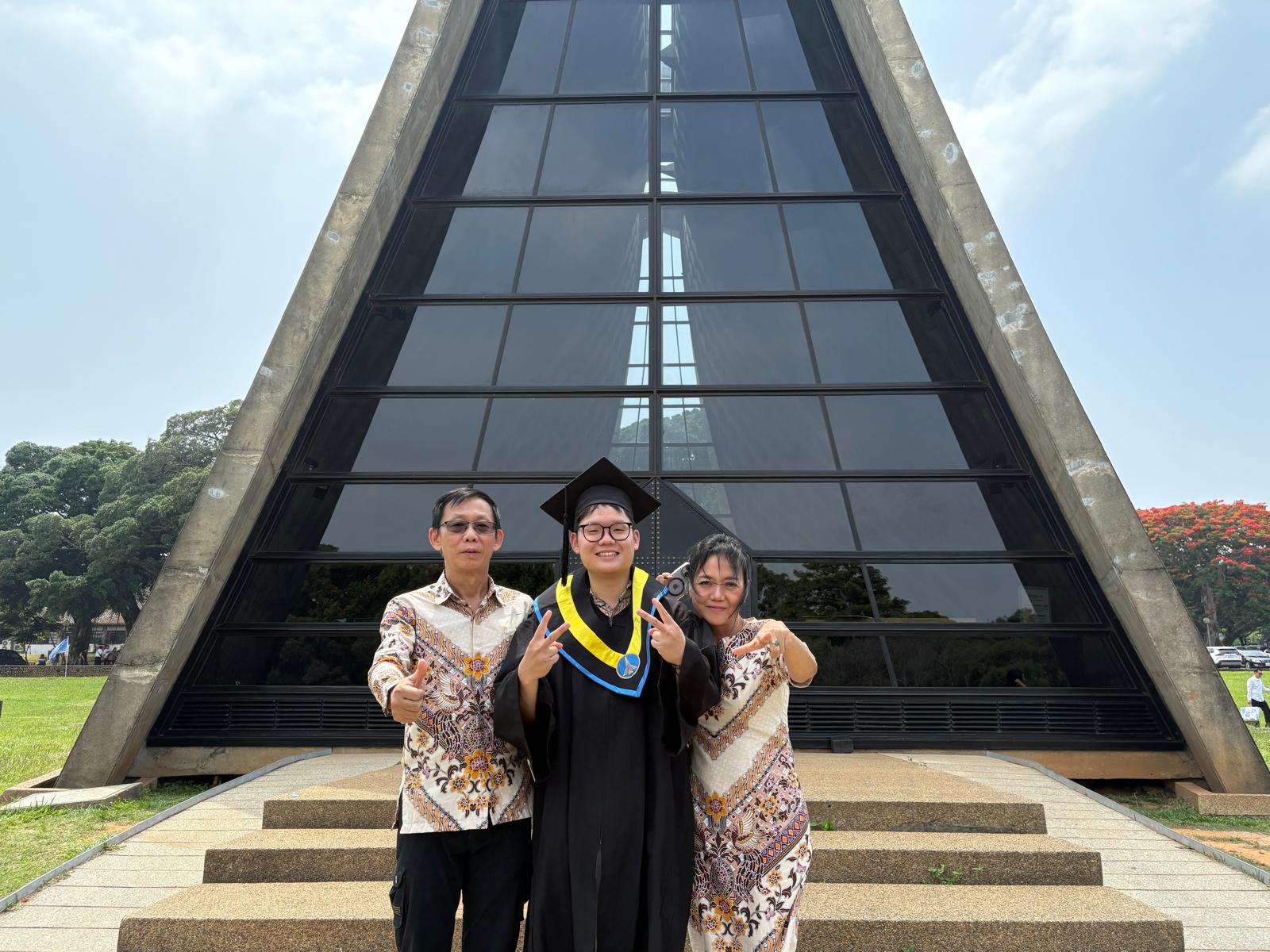 Jonathan in his graduation gown with his family outside a campus chapel